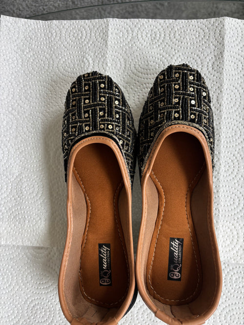 Pair of black and gold patterned flats on a white surface